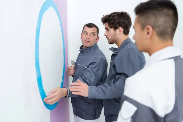 Uomo che mostra agli apprendisti come dipingere un muro — Foto Stock