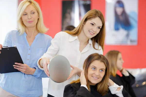Trainee hairdresser showing rear view of hairstyle to customer — Stock Photo, Image