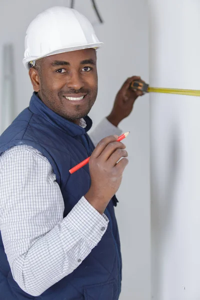 Construtor feliz medindo uma parede — Fotografia de Stock