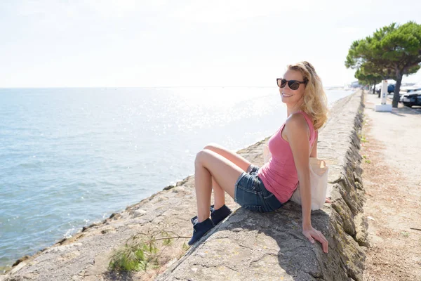 Mujer sentada en la pared de piedra con vistas al mar —  Fotos de Stock