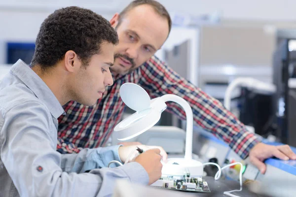 Worker looking through magnifying device to work on electronics board — Stock Photo, Image