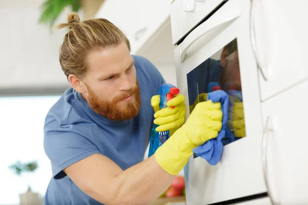 Happy young man in overall cleaning oven — Stock Photo, Image