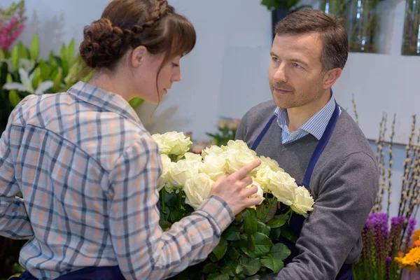 右の花を選ぶ若い女性を助ける男性の花屋 — ストック写真