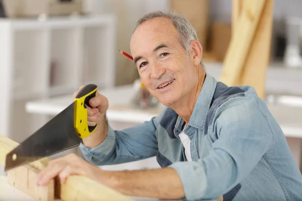 Hombre mayor con una sierra de mano cortando madera —  Fotos de Stock
