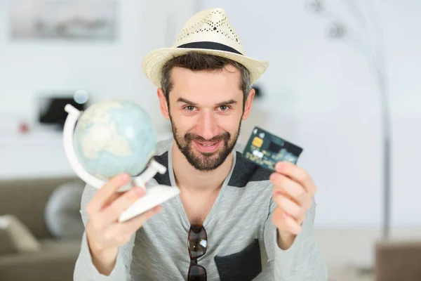 Homme montrant un monde-globe et une carte de crédit — Photo