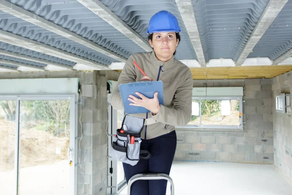 带剪贴板的女建筑工人站在梯子上 — 图库照片