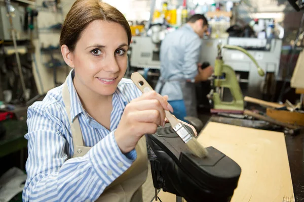 female cobbler using paintbrush on sole of shoe