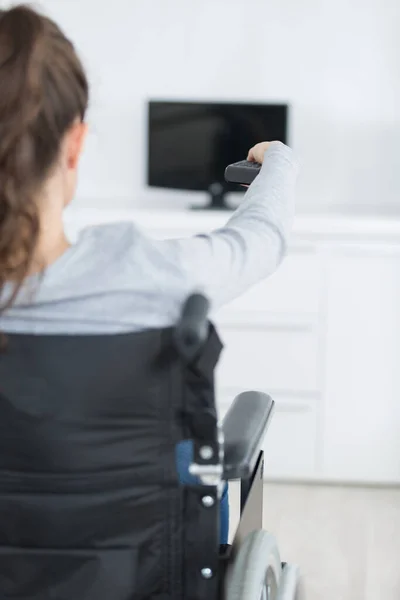 Tekerlekli Sandalyedeki Kadının Uzaktan Kumandayla Televizyon Kanalını Değiştirmesi — Stok fotoğraf