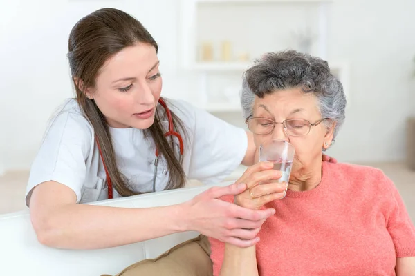 医生给生病的老年妇女一杯水 — 图库照片