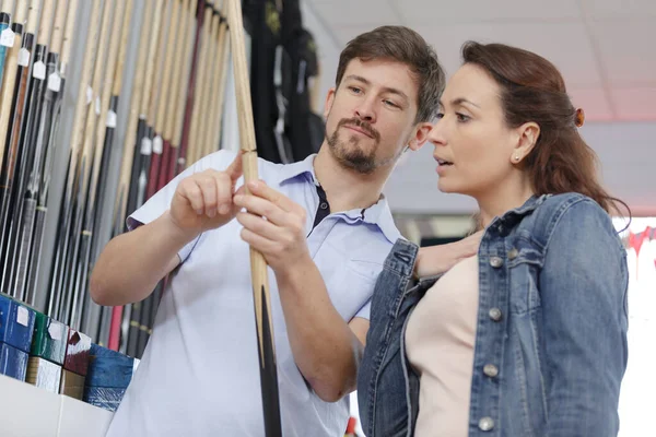 couple choosing billiard cues on the rack