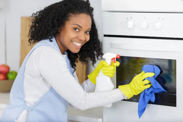 年轻女子在厨房用抹布擦拭烤箱 — 图库照片