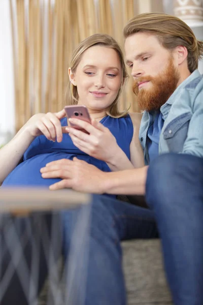 快乐的怀孕夫妇 带着智能手机在客厅里 — 图库照片