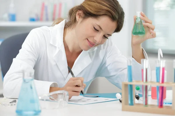 Lächelnde Wissenschaftlerin Mit Einem Reagenzglas Das Notizen Schreibt — Stockfoto