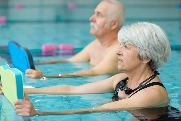 プールボードを持つ高齢者はスイミングプールで運動をします — ストック写真