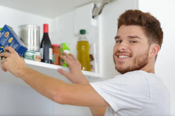 若い男が食器棚に食べ物を置いて — ストック写真