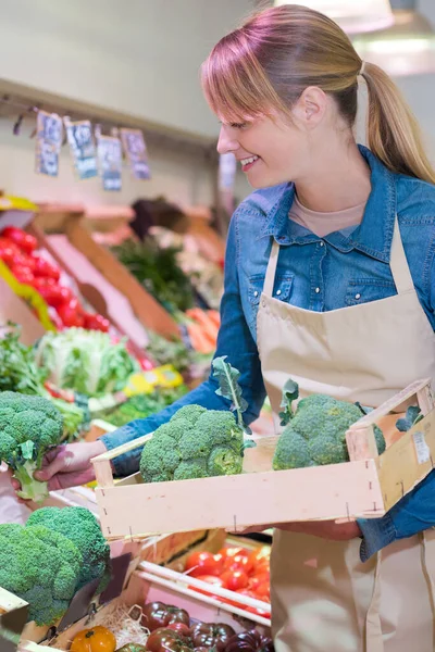 sales assistant restocking broccoli in green grocers