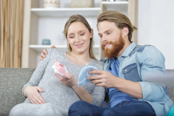 Junger Mann Zeigt Ihrer Schwangeren Frau Babykleidung — Stockfoto