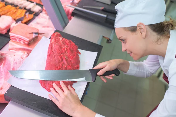 メスの肉屋はナイフで牛肉を切る — ストック写真