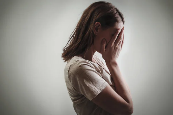 Portrait of depressed woman, covering face with her hands, side view