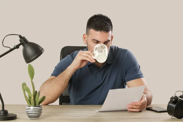 Giovane seduto alla scrivania dell'ufficio e guardando il giornale fare — Foto Stock