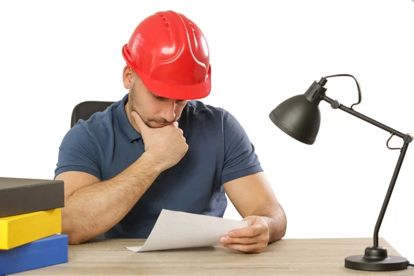 Young man wearing a red helmet in the office and looking at the — Stock Photo, Image