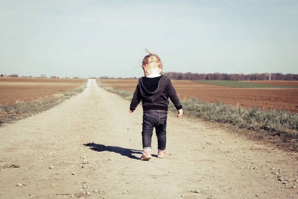 Visão traseira da menina andando em uma estrada de campo empoeirada larga — Fotografia de Stock
