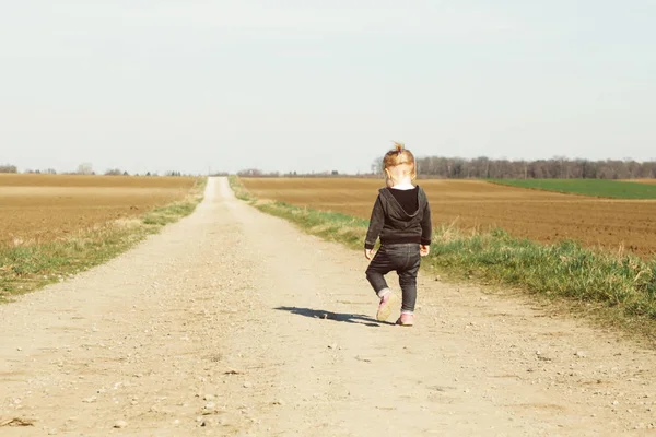 Widok z tyłu Baby Girl chodzenie na szerokim zapylonym kraju drogi — Zdjęcie stockowe