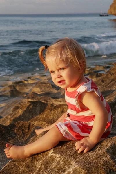 一个穿着红白相间衣服的女婴坐在岩石海岸上 在户外呆上一段时间对孩子们来说很重要 — 图库照片