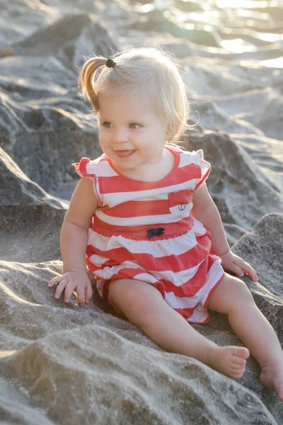 一个穿着红白相间衣服的女婴坐在岩石海岸上 在户外呆上一段时间对孩子们来说很重要 — 图库照片