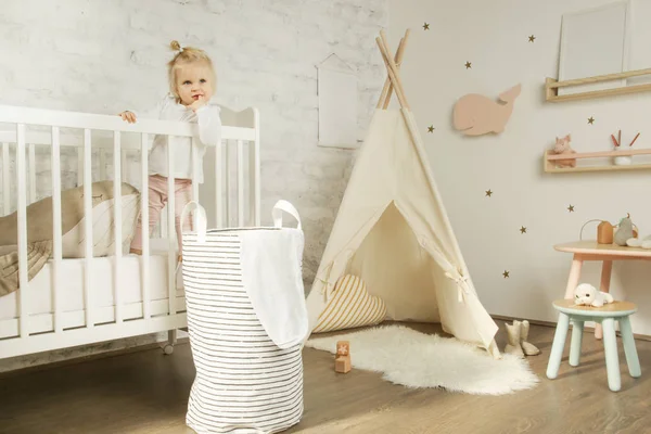 Adorable cheerful baby girl in the crib in the nursery room