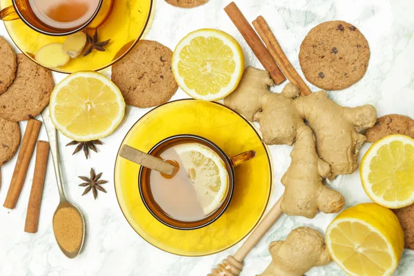 Ginger tea in a cup with ginger roots and lemon on marble textured background, top view. A healthy lifestyle, anti-flu and anti-inflammatory concept.