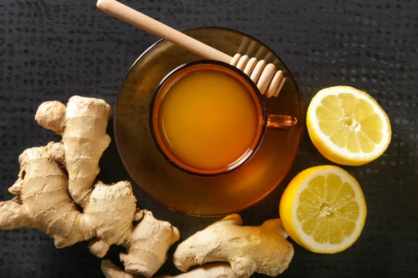 Ginger tea in a cup with ginger roots and lemon on the dark background. A healthy lifestyle, anti-flu and anti-inflammatory concept.