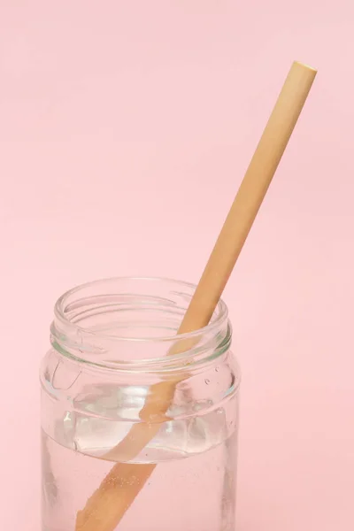 Bamboo straw in a glass of  water on the pink background, Reusable bamboo straws as an alternative for single-use plastic straws, healthy and sustainable lifestyle concept