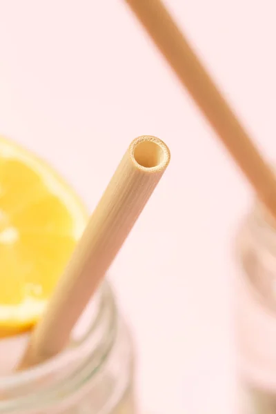 Bamboo straw in a glass of lemon water on the pink background, Reusable bamboo straws as an alternative for single-use plastic straws, healthy and sustainable lifestyle concept