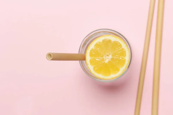 Bamboo straw in a glass of lemon water on the pink background, Reusable bamboo straws as an alternative for single-use plastic straws, healthy and sustainable lifestyle concept