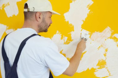 Macun bıçağıyla duvar ören adam, görüntüyü kapatın. Duvar yüzeyinin sabitlenmesi ve boyama için hazırlık.