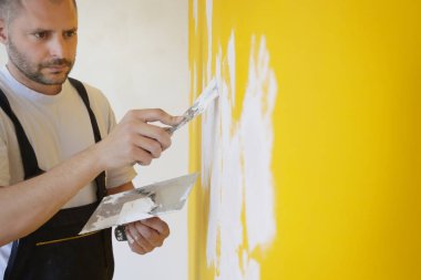 Macun bıçağıyla duvar ören adam, görüntüyü kapatın. Duvar yüzeyinin sabitlenmesi ve boyama için hazırlık.