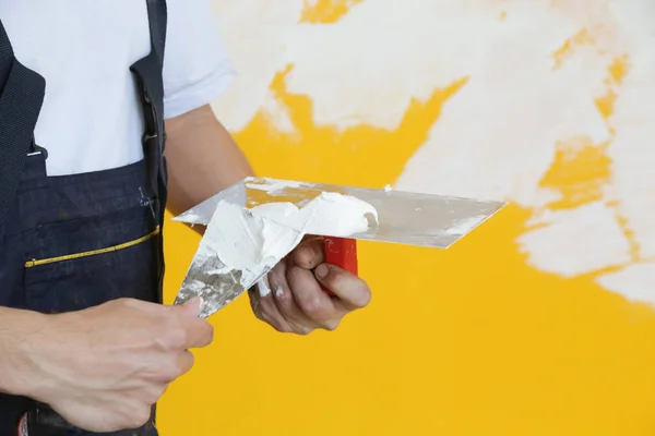 Man plastering wall with putty-knife, close up image. Fixing wall surface and preparation for painting.