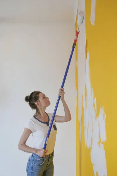 Γυναίκα Ζωγραφική Λευκό Χρώμα Πάνω Από Ένα Κίτρινο Τοίχο — Φωτογραφία Αρχείου