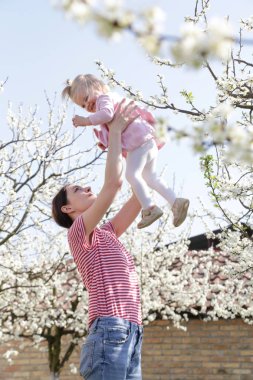 Genç mutlu anne, sevimli bebeğini kucağına alıp oynuyor. Açık hava çekimi, aile hayatı konsepti.
