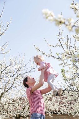 Genç mutlu anne, sevimli bebeğini kucağına alıp oynuyor. Açık hava çekimi, aile hayatı konsepti.