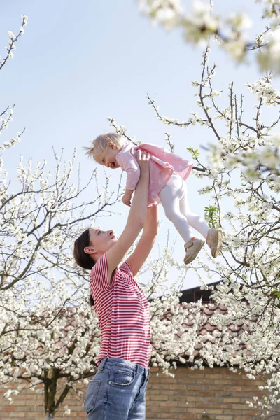 Genç mutlu anne, sevimli bebeğini kucağına alıp oynuyor. Açık hava çekimi, aile hayatı konsepti.