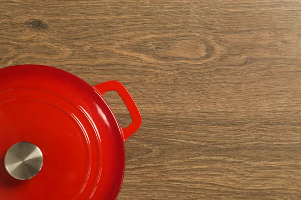 Top view of red enameled iron stockpot on wooden background