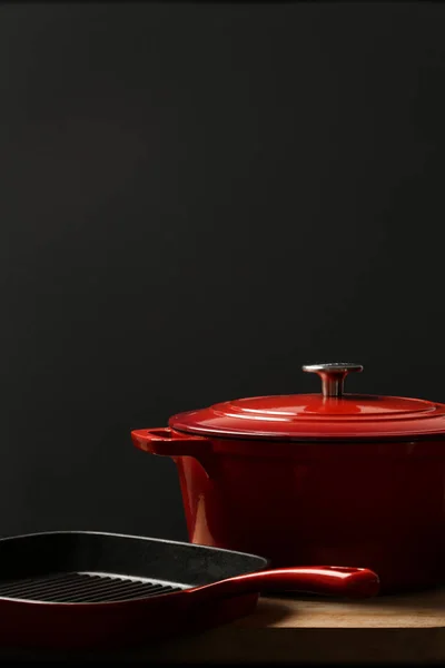 Cookware set: Red enameled cast iron pot, saucepan on black background