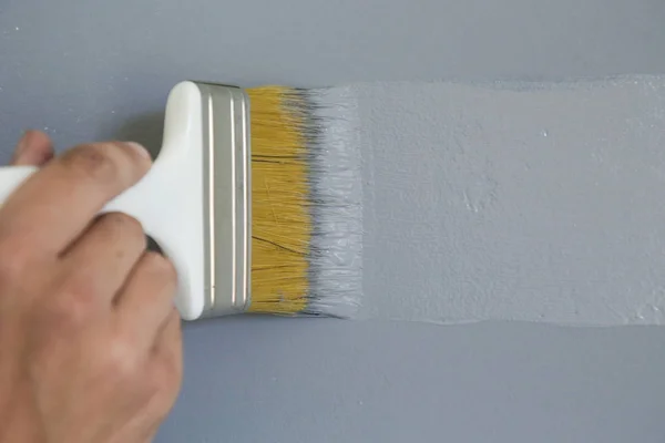 灰色の壁にペンキブラシで絵を描く男 — ストック写真