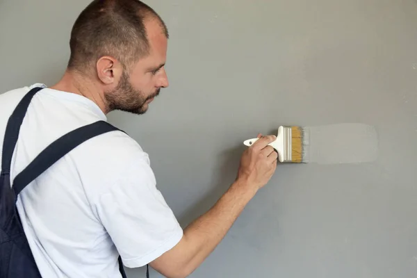 Человек Рисует Кистью Над Серой Стеной — стоковое фото