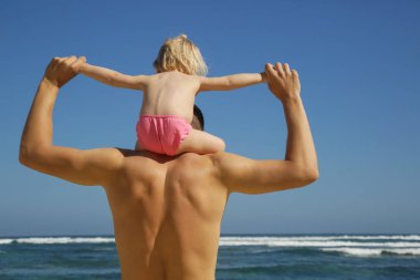 Plajda babamın omuzlarında oturan bir bebek kız arka görünümü, Aile yaz tatil kavramı.