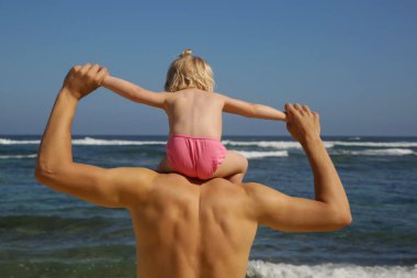 Plajda babamın omuzlarında oturan bir bebek kız arka görünümü, Aile yaz tatil kavramı.
