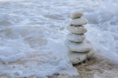 Balance zen stones pyramid on pebble beach with a splashing wave. Stability, balance, and harmony concept clipart