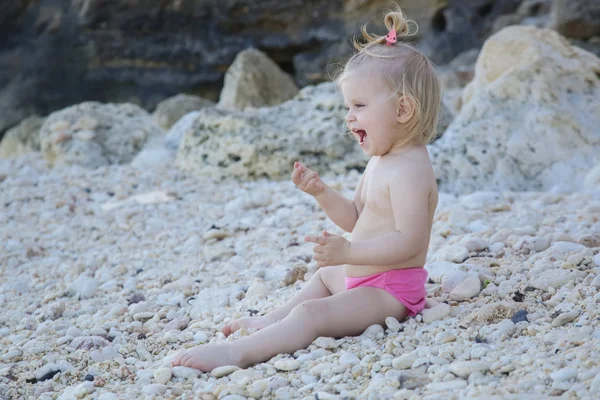 Candid portrait of a cute blonde baby girl enjoying a day at the rocky beach
